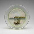 A close-up view of a clear convex glass  with a green rim, showing a coastal scene with cliffs in the background painted in watercolour