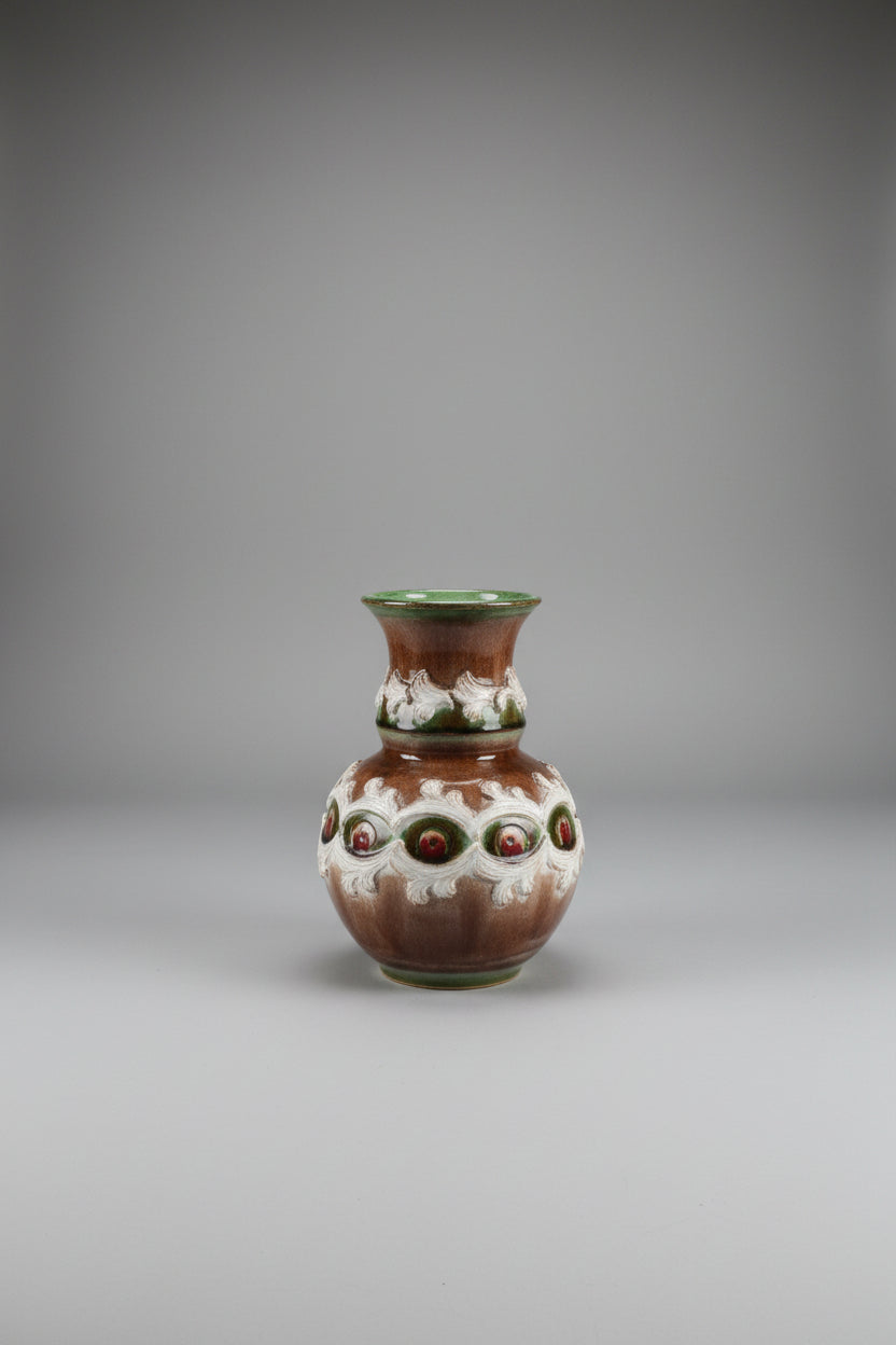 An ornate earthenware vase with a brown and white marbled pattern, featuring three raised circular medallions with red and green accents, displayed  against a plain light background.