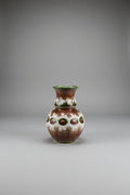 An ornate earthenware vase with a brown and white marbled pattern, featuring three raised circular medallions with red and green accents, displayed  against a plain light background.