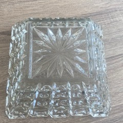 A clear cut-glass bowl base with a starburst pattern in the center, resting on a brown wood-grain surface.